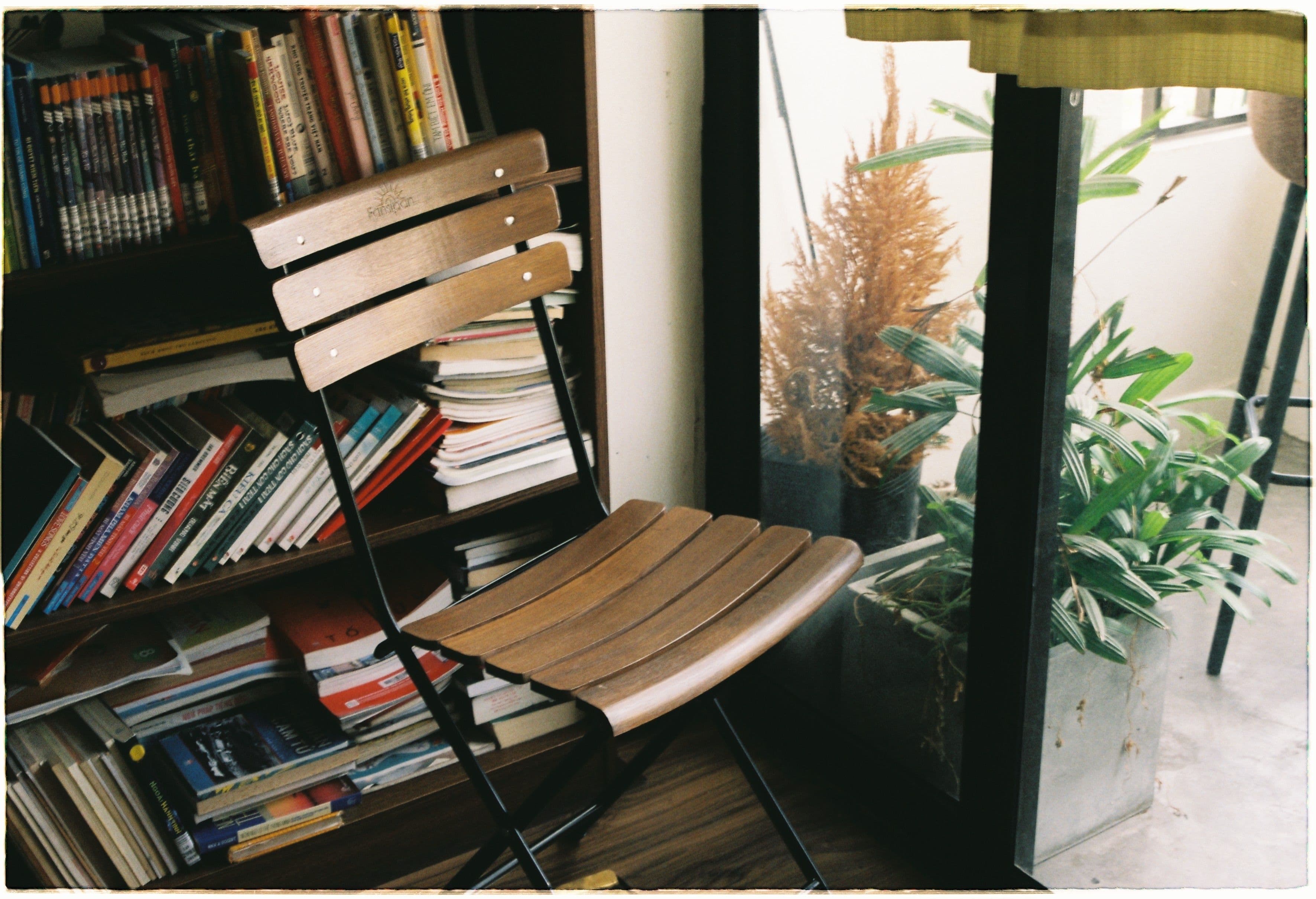 A quiet reading nook with a wooden chair beside a full bookshelf, soft natural light and plants nearby